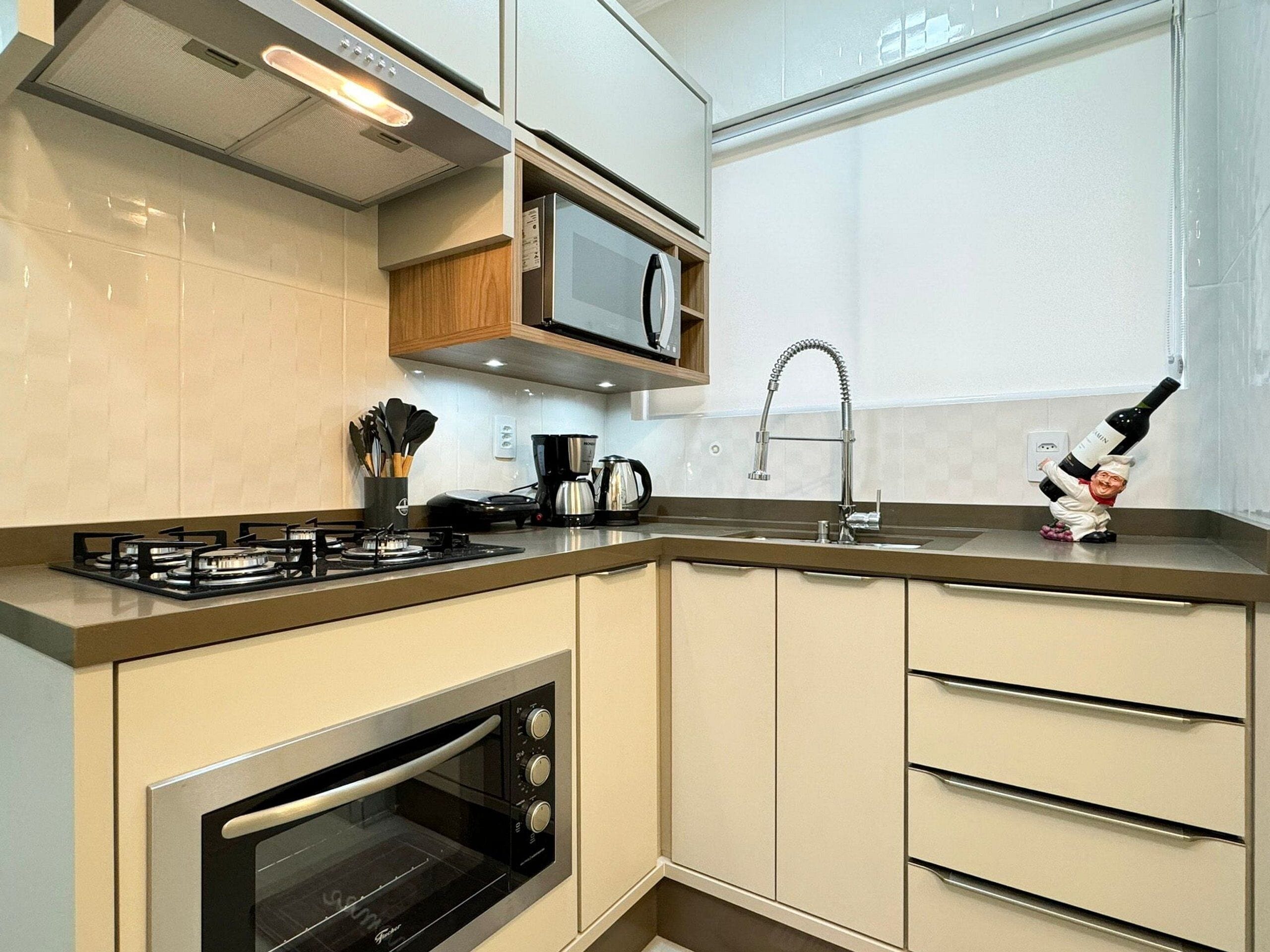 Een moderne keuken met een ingebouwde magnetron, gasfornuis, oven en een roestvrijstalen spoelbak.