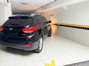 Un coche negro estacionado en un estacionamiento con paredes de azulejos blancos y detalles en baldosas amarillas y negras.
