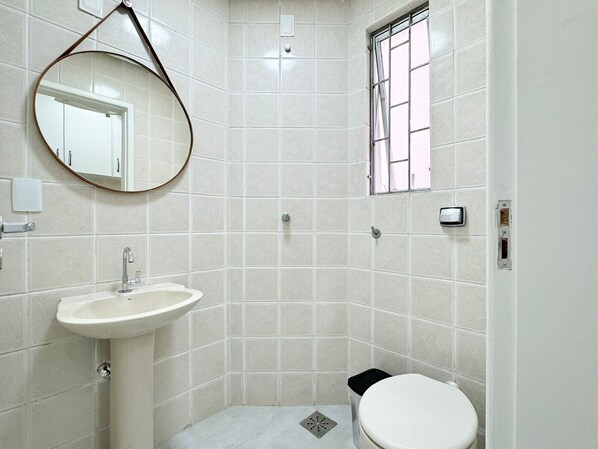 A bathroom with a white sink, a toilet, a mirror, and a window with bars.
