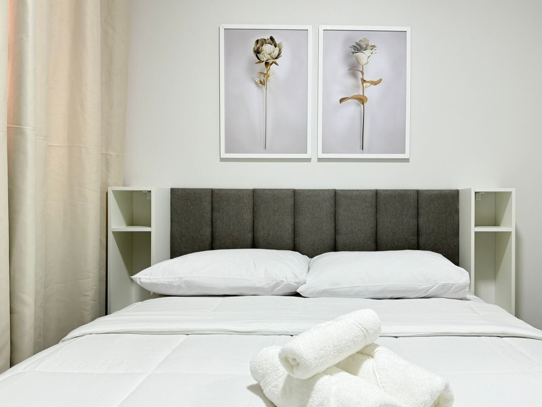 A neatly made bed with white linens, a grey upholstered headboard, and two wall-mounted picture frames with floral designs.