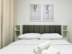 Una cama bien hecha con sábanas blancas, un cabecero tapizado de gris y dos marcos de cuadros en la pared con motivos florales.