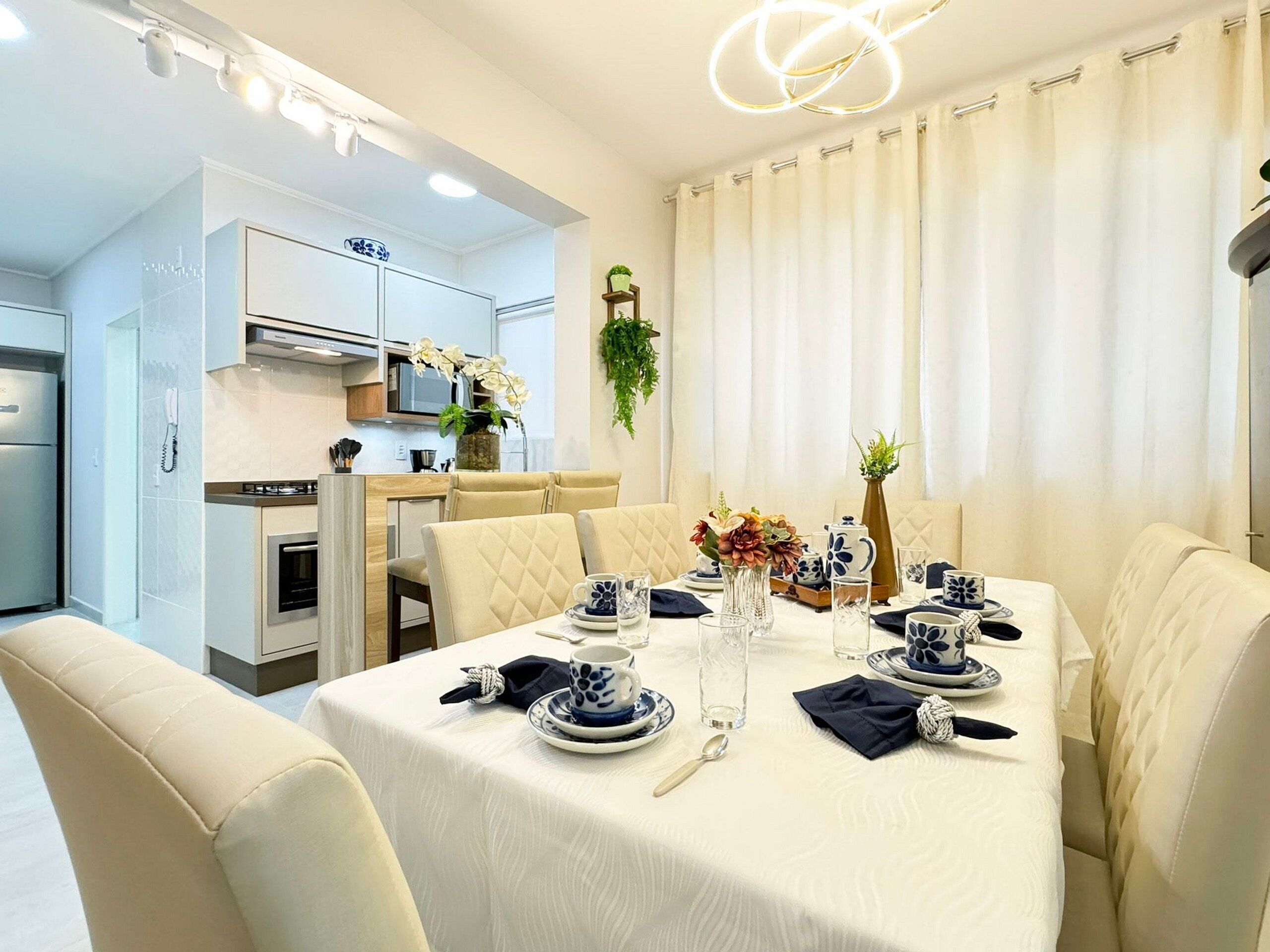 Zona pranzo con tavolo apparecchiato per quattro persone, cucina sullo sfondo e lampadario moderno.