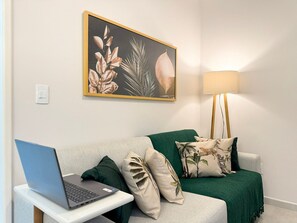 A room with a green sofa, a laptop on a small table, a lamp, and a framed plant artwork on the wall. - Res. Villa de Collina-Centro de Floripa (Florianopolis)