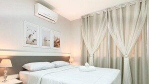 A hotel room with a neatly made bed, two bedside lamps, a wall-mounted air conditioner, and a set of curtains. - Res. Villa de Collina-Centro de Floripa (Florianopolis)