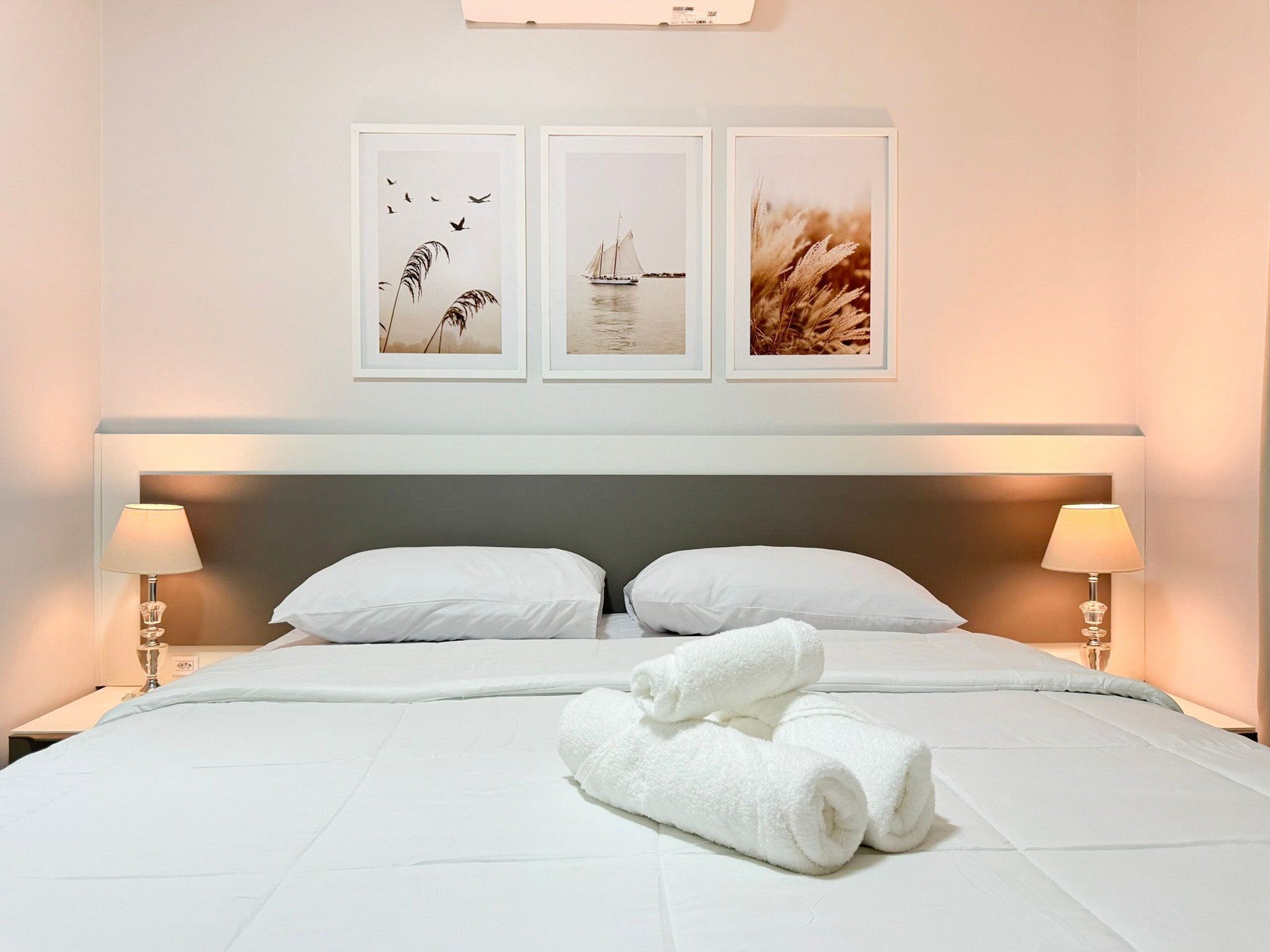 Habitación de hotel con una cama, dos almohadas, una mesita de noche con lámpara y tres cuadros enmarcados en la pared.