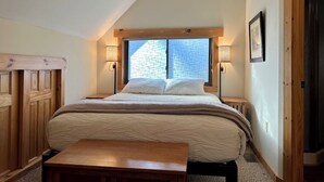 Ein Schlafzimmer mit einem großen Bett, zwei Nachttischlampen, einer hölzernen Bank und einem Fenster mit Blick auf eine Ziegelwand.
