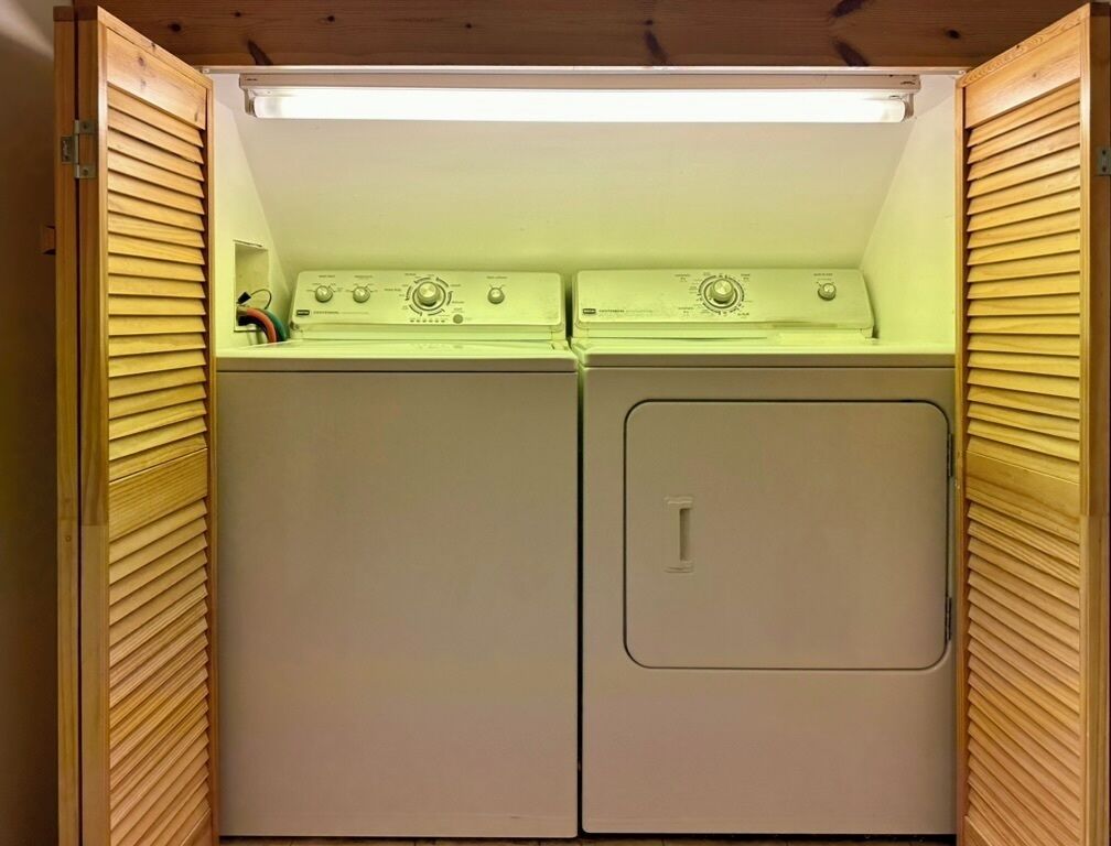 Un lavadero pequeño con dos lavadoras y secadoras apiladas, paneles de madera y una luz fluorescente arriba.