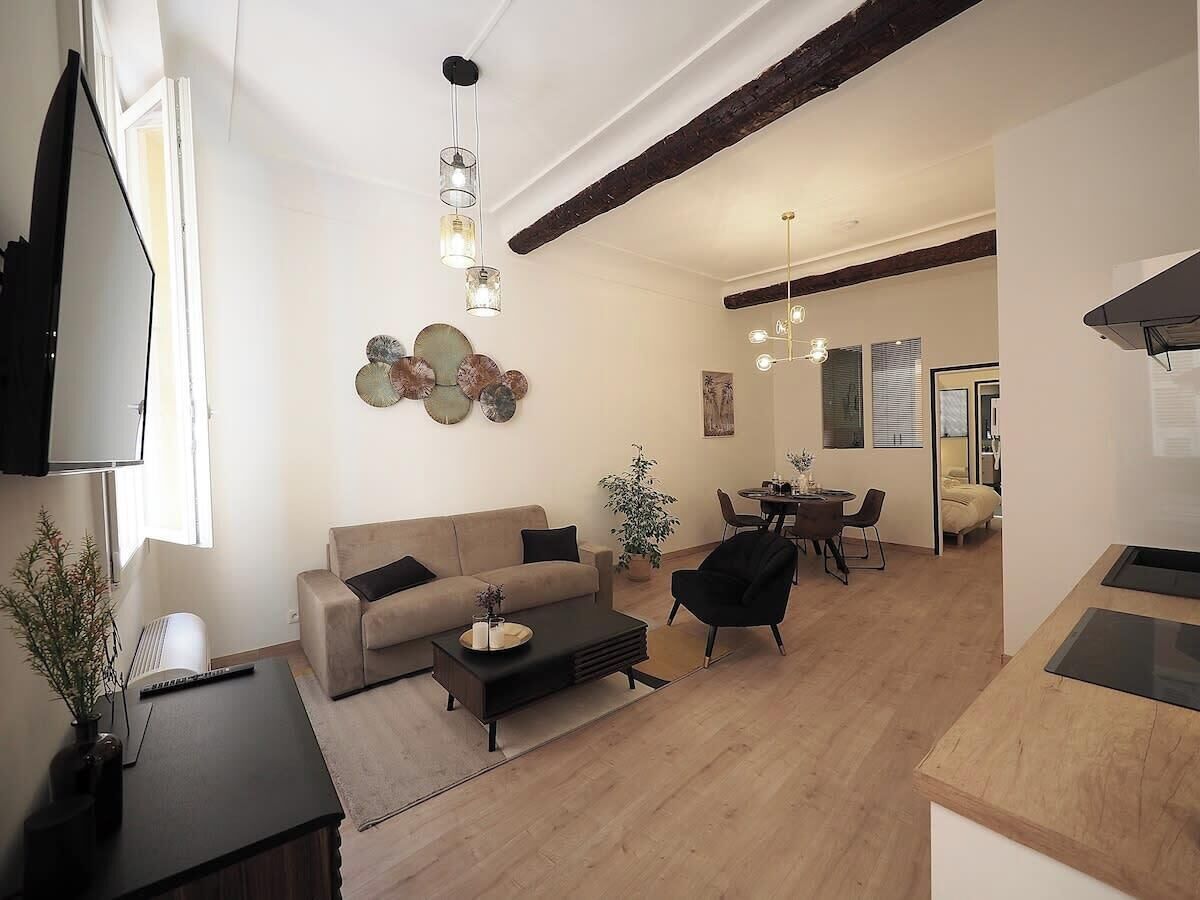 A spacious living area with a sofa, coffee table, and dining table. There is a TV mounted on the wall and a plant in the corner.