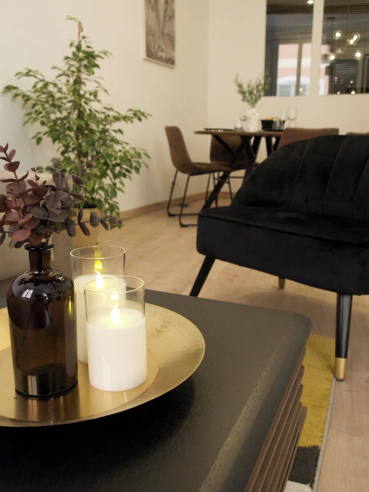 A modern living room with a black sofa, a dining table with chairs, and a potted plant.