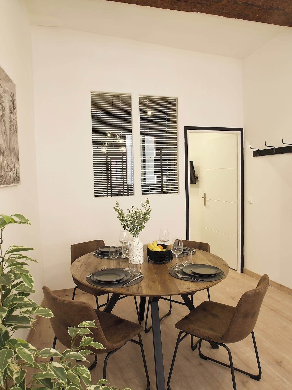 Uma sala de jantar com uma mesa redonda, quatro cadeiras e um vaso com flores.