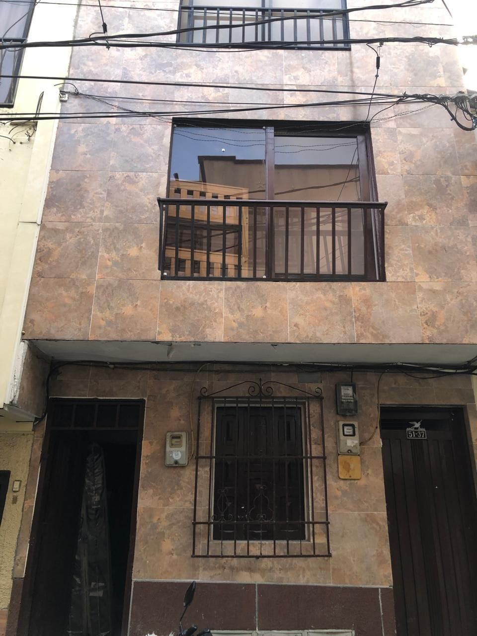 Un edificio de dos pisos con un balcón, una ventana con reja de metal y una puerta con un número.