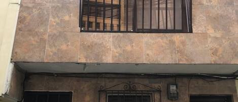 Un edificio de dos pisos con un balcón, una ventana con reja de metal y una puerta con un número.