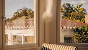 A corner room with a striped sofa, a small round table, and a window with a view of buildings and trees. - Outsite Vilamoura - Work, Connect, Explore (Loule)