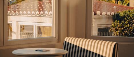 A corner room with a striped sofa, a small round table, and a window with a view of buildings and trees.