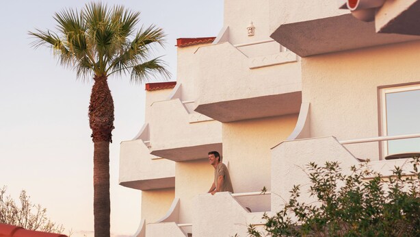 A building with a unique architectural design featuring multiple balconies and a palm tree in the foreground. - Outsite Vilamoura - Work, Connect, Explore (Loule)
