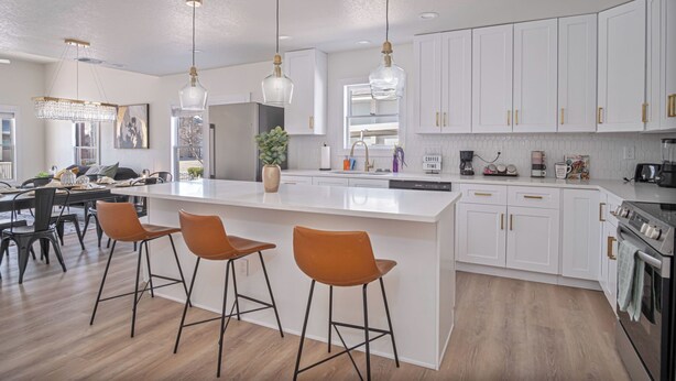 Una cocina moderna con armarios blancos, una isla grande con taburetes de bar, iluminación colgante y un horno empotrado.