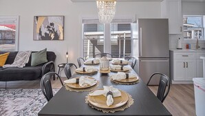 Un moderno comedor con una mesa de madera oscura dispuesta para seis personas, rodeada de sillas negras. Un candelabro cuelga encima, y un cuadro abstracto de gran tamaño adorna la pared.