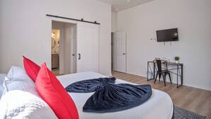 Un dormitorio con cama, escritorio, televisor y puerta que da a otra habitación.