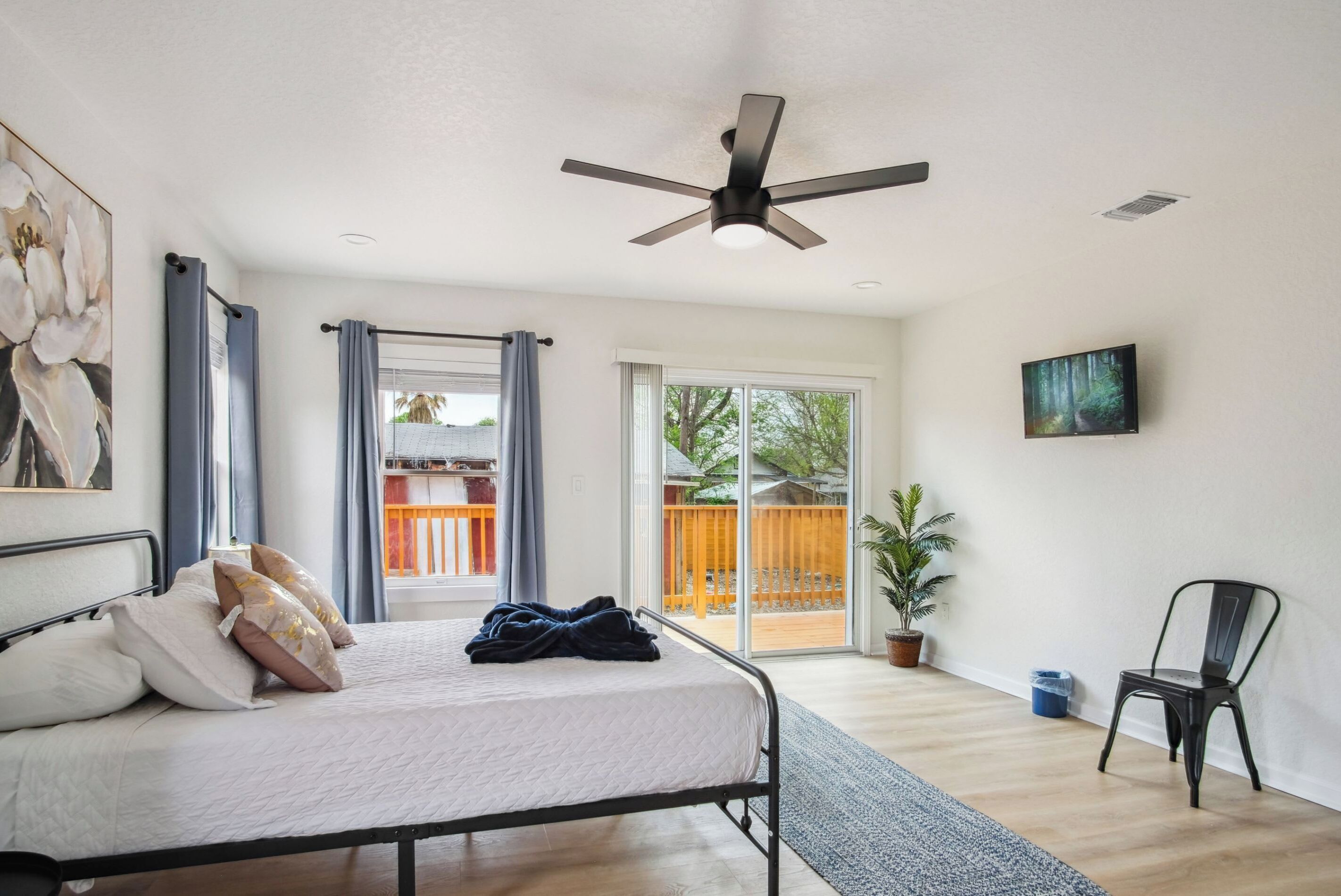 Ein Schlafzimmer mit Bett, Deckenventilator, einer Schiebetür zu einem Außenbereich, einem Topf mit Pflanze und einem Sessel.