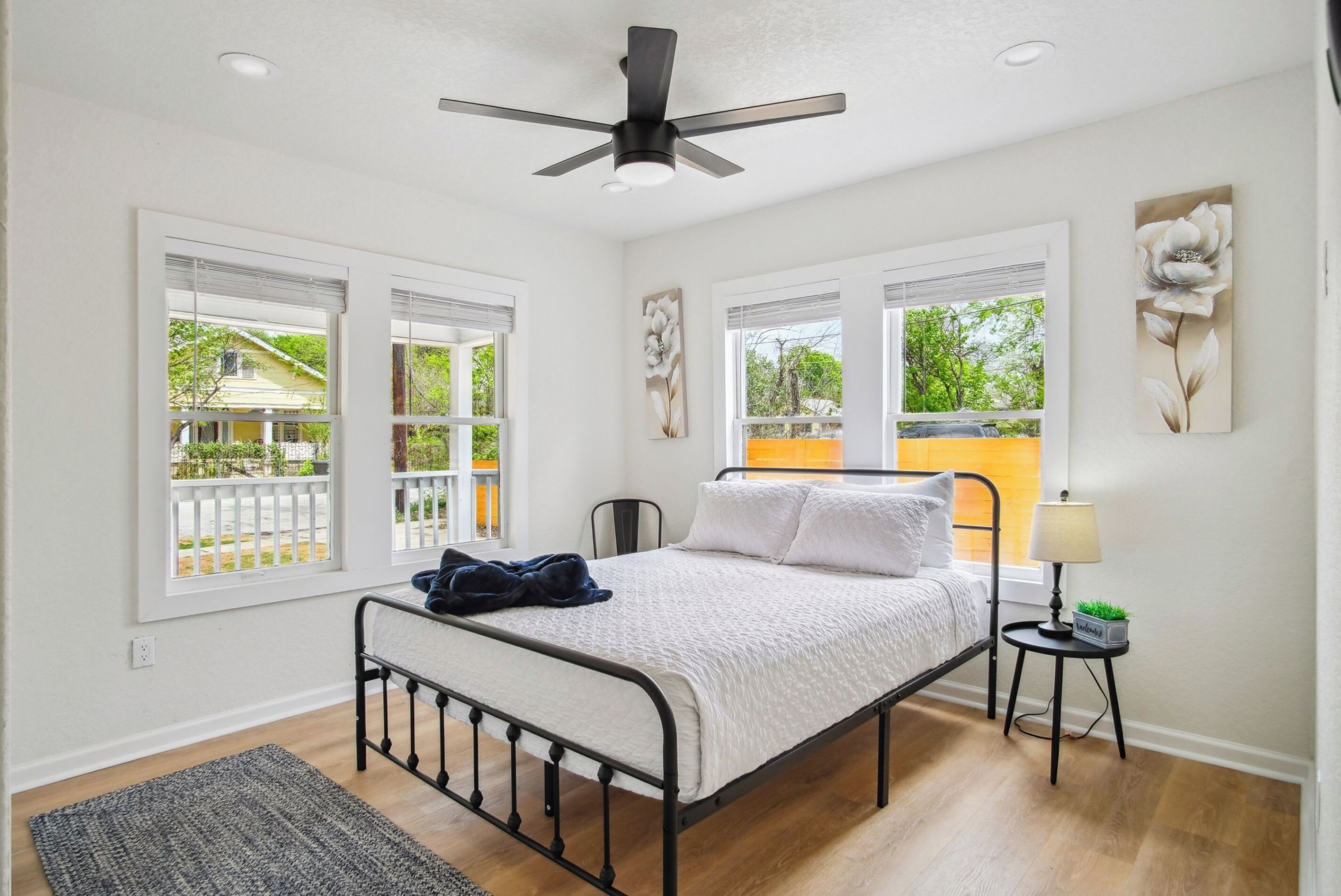 A bedroom with a bed, a ceiling fan, a nightstand, and large windows.