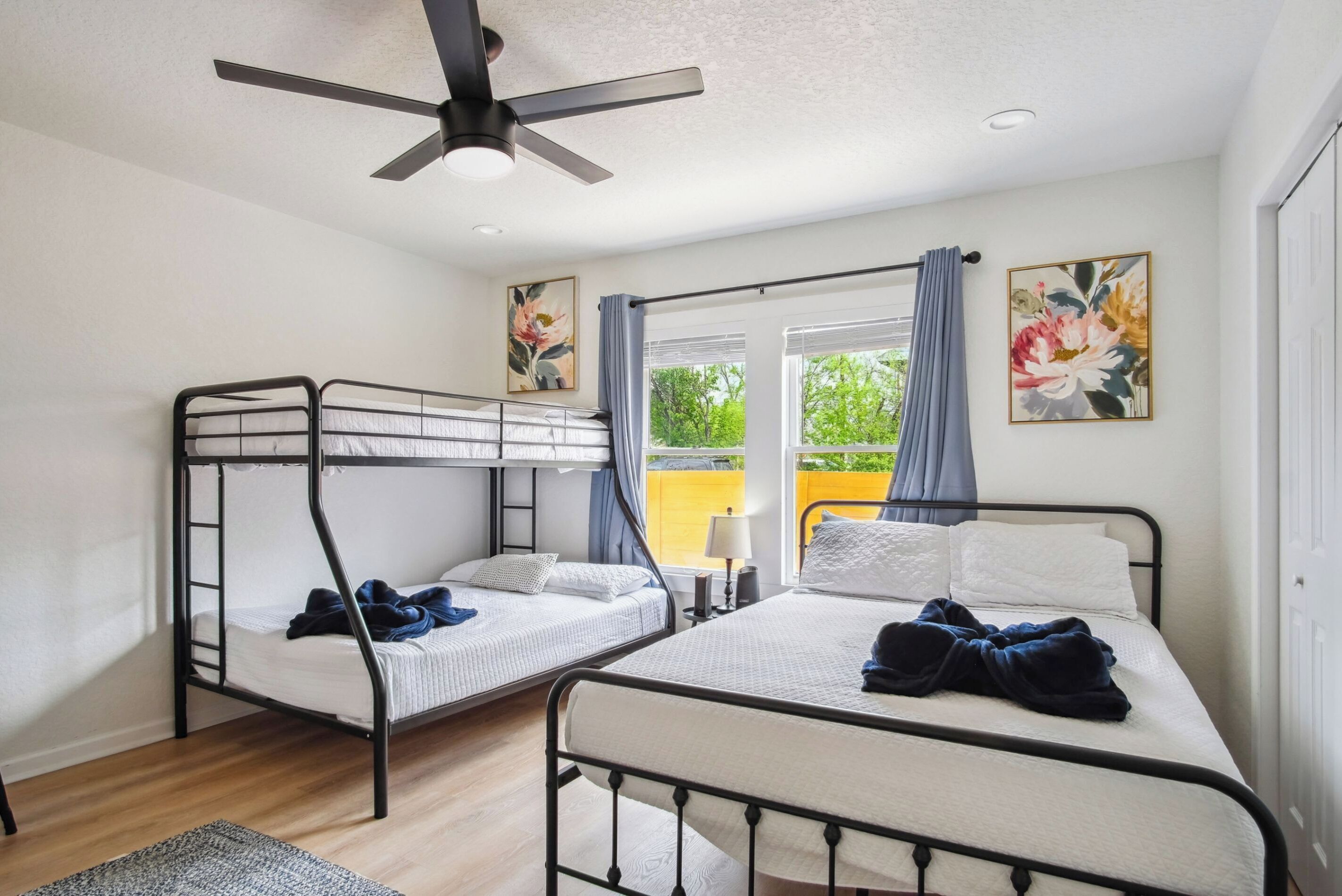Ein Zimmer mit Etagenbetten, Deckenventilator, Fenster mit Vorhängen und zwei Bildern an der Wand.