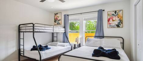 Ein Zimmer mit Etagenbetten, Deckenventilator, Fenster mit Vorhängen und zwei Bildern an der Wand.