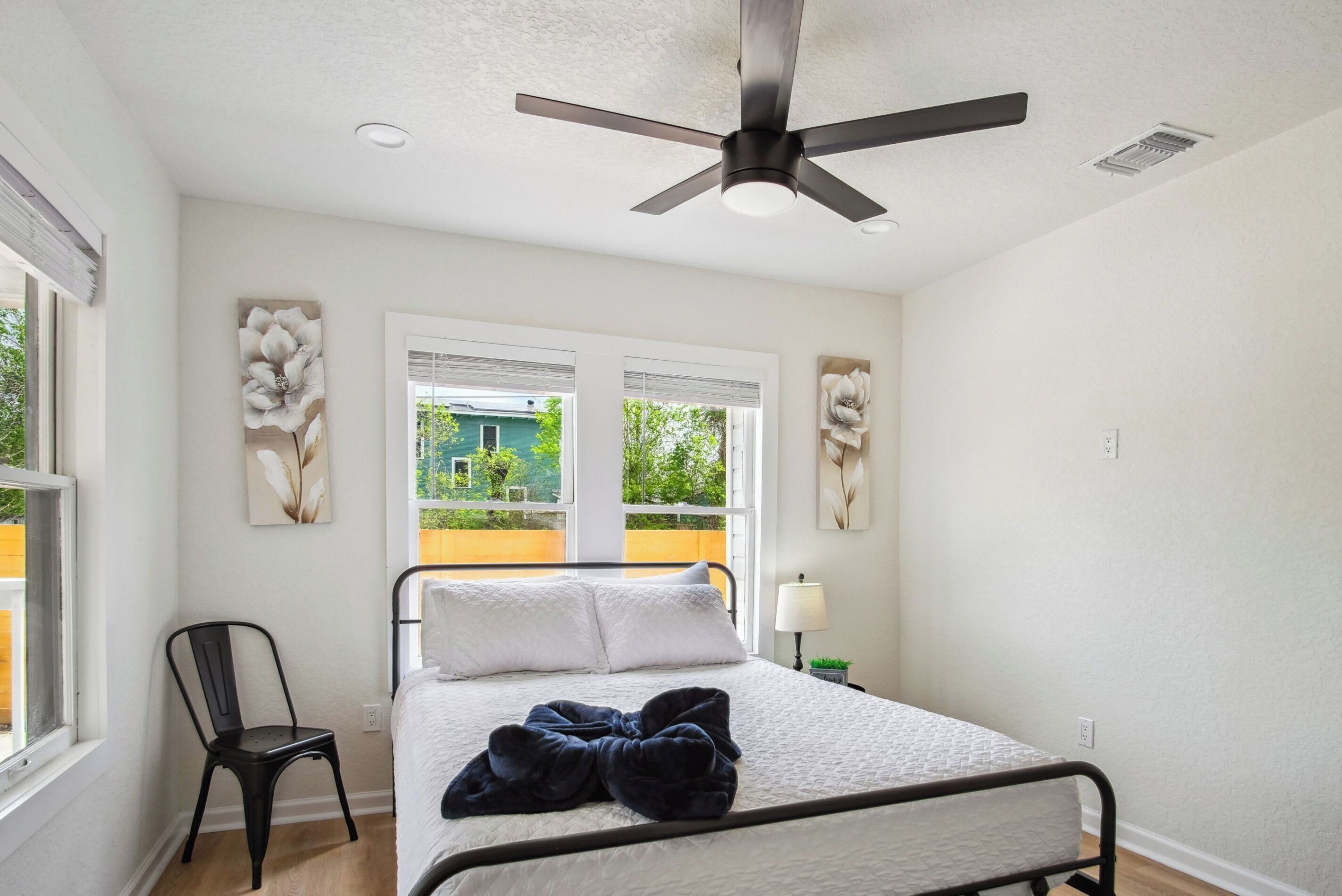 A bedroom with a bed, a ceiling fan, and two windows with blinds.