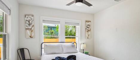 A bedroom with a bed, a ceiling fan, and two windows with blinds.