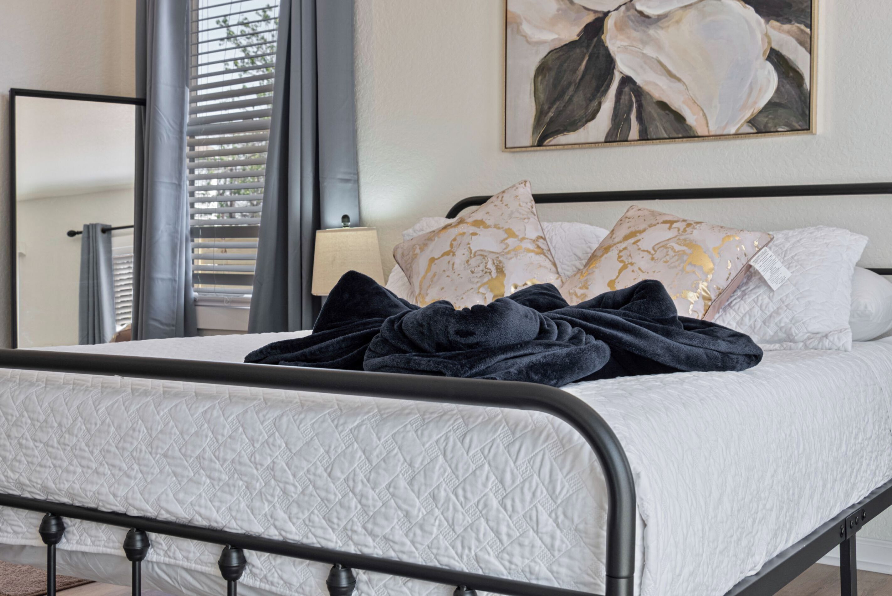 Een opgemaakt bed met een witte gewatteerde sprei, een donkerblauwe deken en decoratieve kussens met gouden accenten.