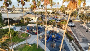 A playground with slides and climbing structures, surrounded by palm trees and a parking lot. - Oceanfront Escape - Steps to Beach - Stunning Views & Balcony (Redondo Beach)