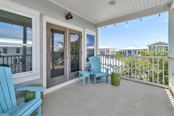 A covered porch with a blue Adirondack chair, a small table, and a green planter. - Dragonfly Dreams 30A (Panama City Beach)