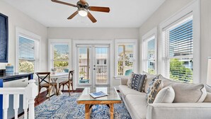 A spacious living area with a ceiling fan, a glass coffee table, a sofa, and a dining area with chairs and a table. - Dragonfly Dreams 30A (Panama City Beach)