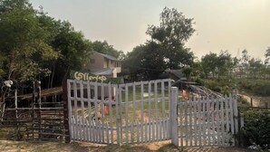 A gated property with a wooden fence, a house in the background, and surrounding greenery. - Golok Riverside Retreat (Bolpur)