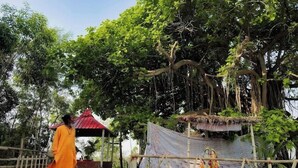 A temple with a thatched roof, a statue of a deity, and a person in traditional attire. - Golok Riverside Retreat (Bolpur)