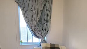 Ein Schlafzimmer mit zwei Betten, einem Fenster mit Vorhängen und Blick ins Freie.
