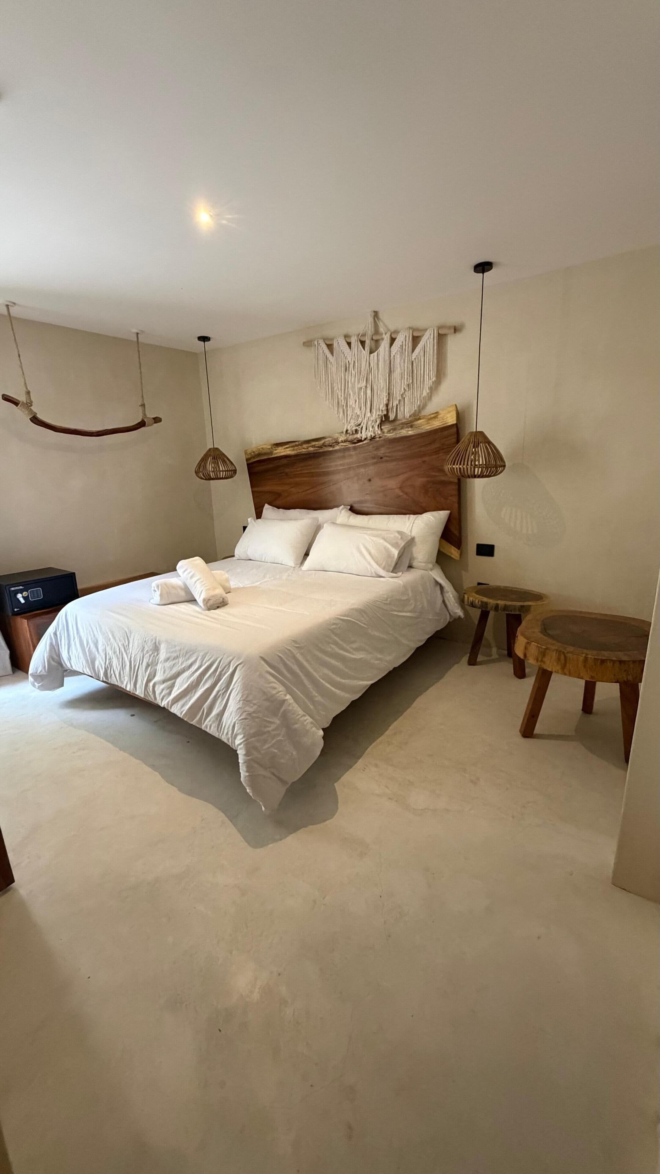 A bedroom with a bed, bedside tables, a macrame wall hanging, and hanging light fixtures.