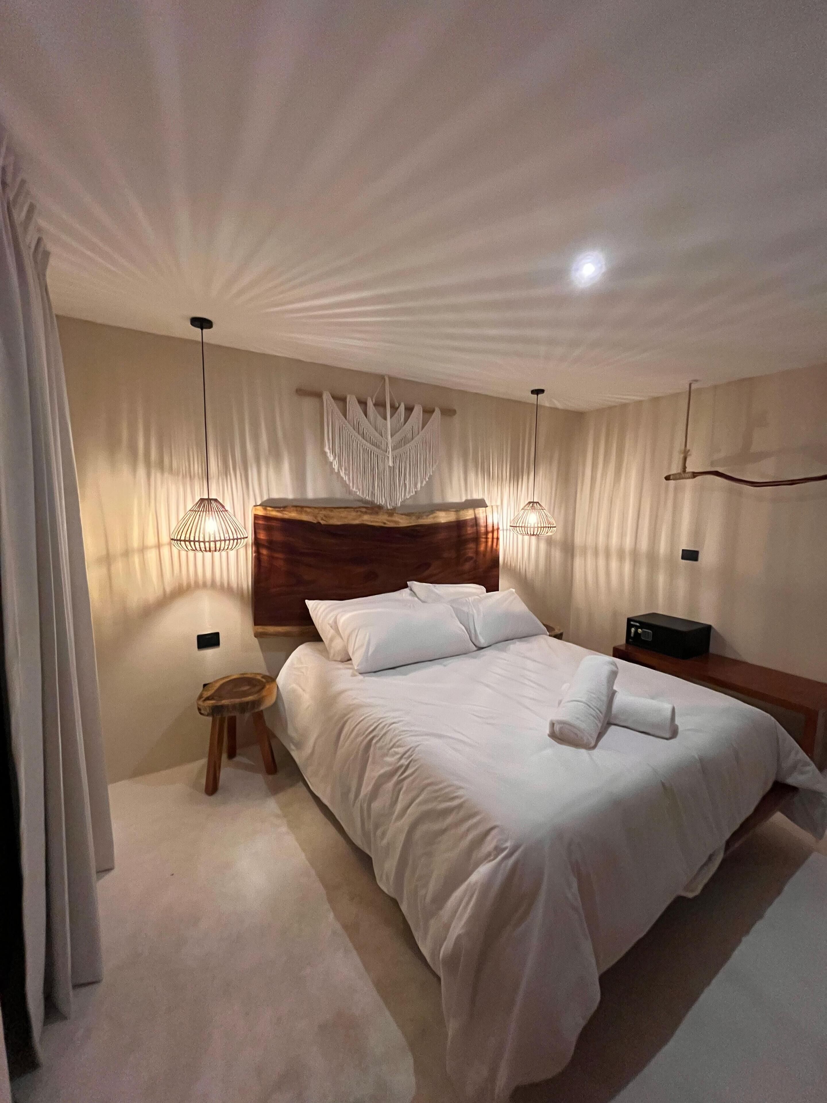 Un dormitorio moderno con una cama grande, cabecera de madera, mesitas de noche y una lámpara colgante.