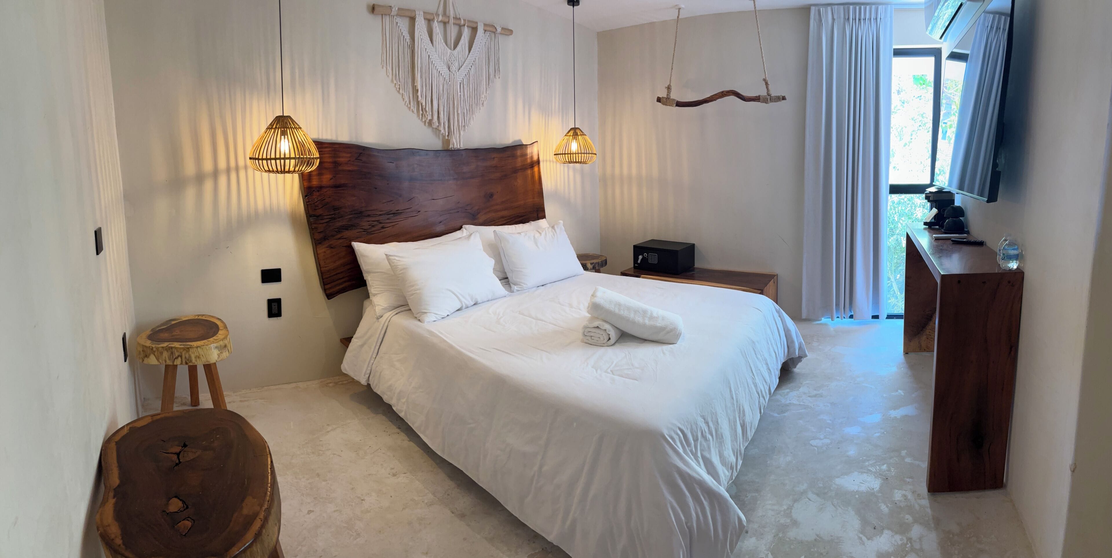 Camera da letto con una testiera in legno, biancheria bianca, un comodino con una radio e una decorazione in macramè appesa.
