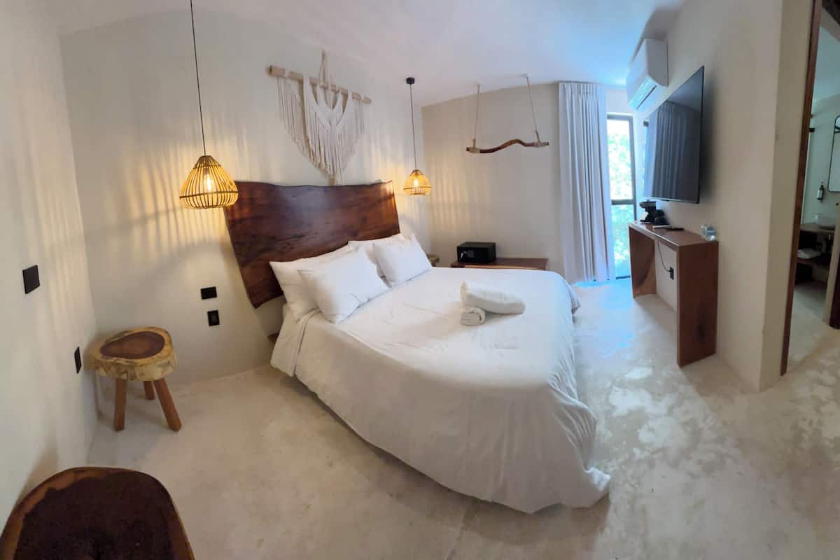 A bedroom with a large bed, bedside lamps, a TV, and a small wooden stool.