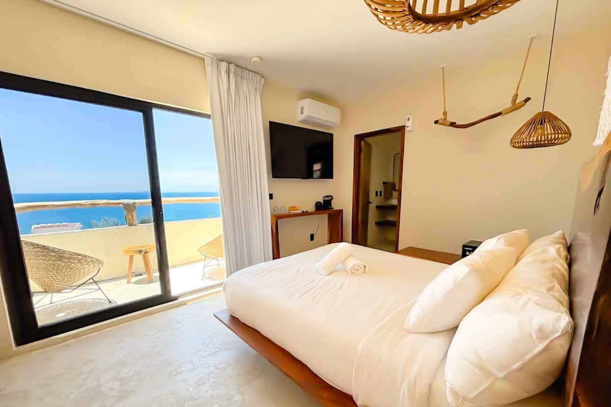 A bedroom with a large bed, a view of the beach, and a balcony.
