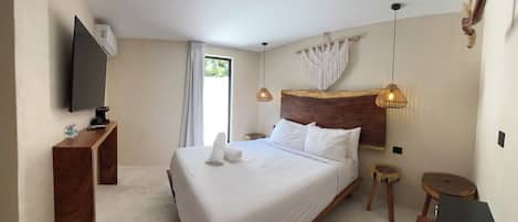 Un dormitorio con una cama grande, televisor, mesita de noche de madera, una pequeña mesa redonda y una lámpara colgante.