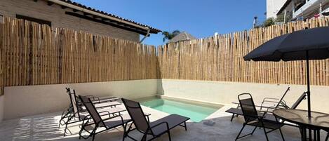 A backyard with a swimming pool, outdoor furniture, and a bamboo fence.