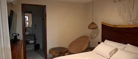 Una habitación de hotel con una cama grande, cabecera de madera, mesita de noche, una silla y una lámpara colgante.