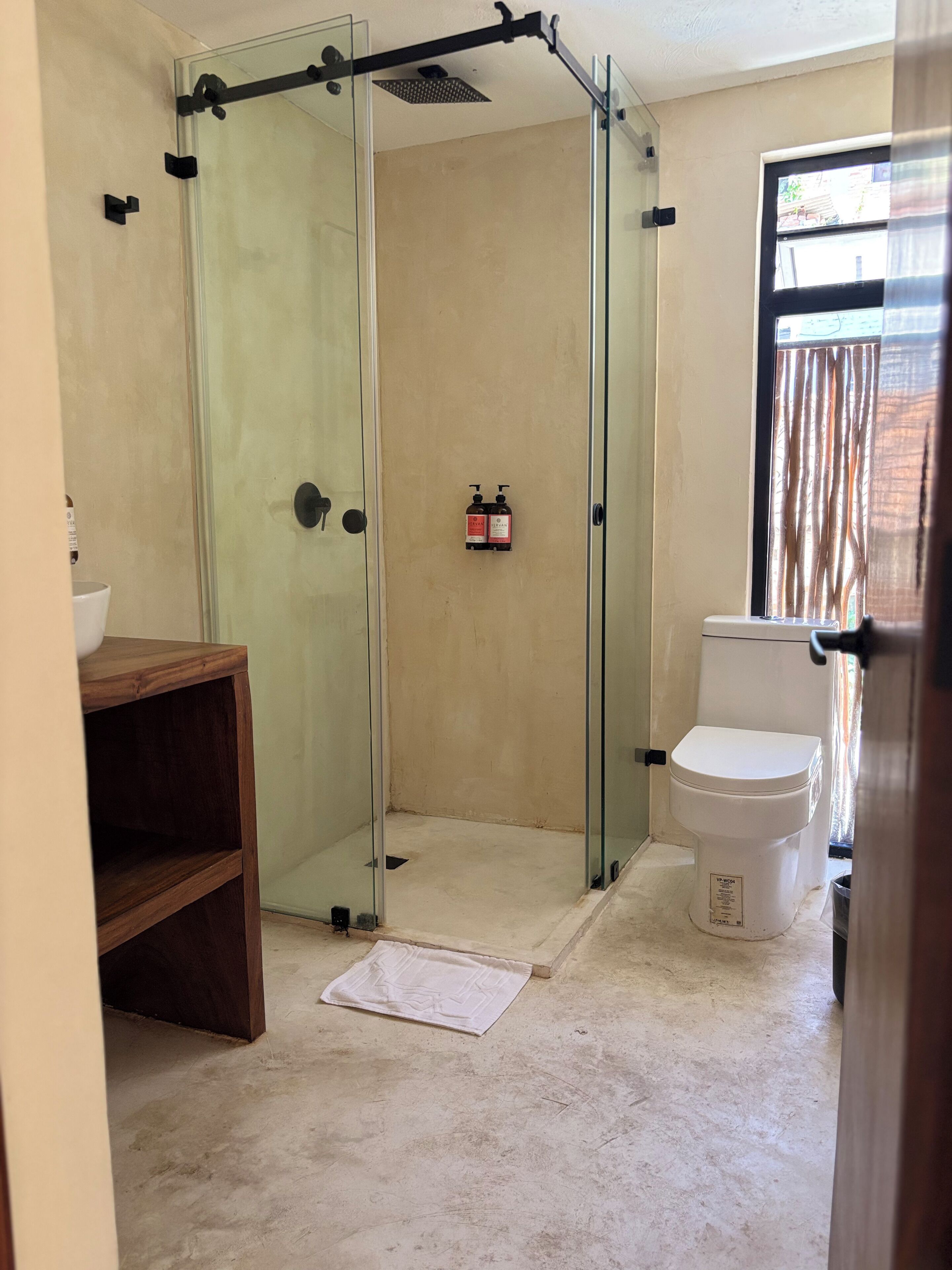 Une salle de bain avec une douche à parois de verre, des toilettes blanches et un meuble-lavabo en bois.