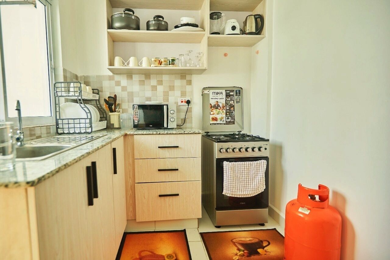 Cocina compacta con microondas, estufa y cocina a gas. Cuenta con gabinetes de madera, un lavamanos y un cilindro de gas.