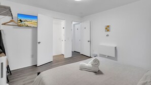 Une chambre d’hôtel moderne, dotée d’un lit, d’un téléviseur fixé au mur, d’un plancher en bois et d’un couloir menant à d’autres chambres.