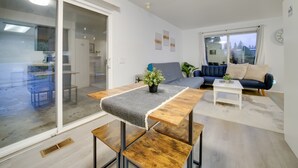 Un salon moderne doté d’une porte-fenêtre coulissante donnant sur un balcon, d’une table à manger en bois, d’un canapé et d’une table basse blanche.