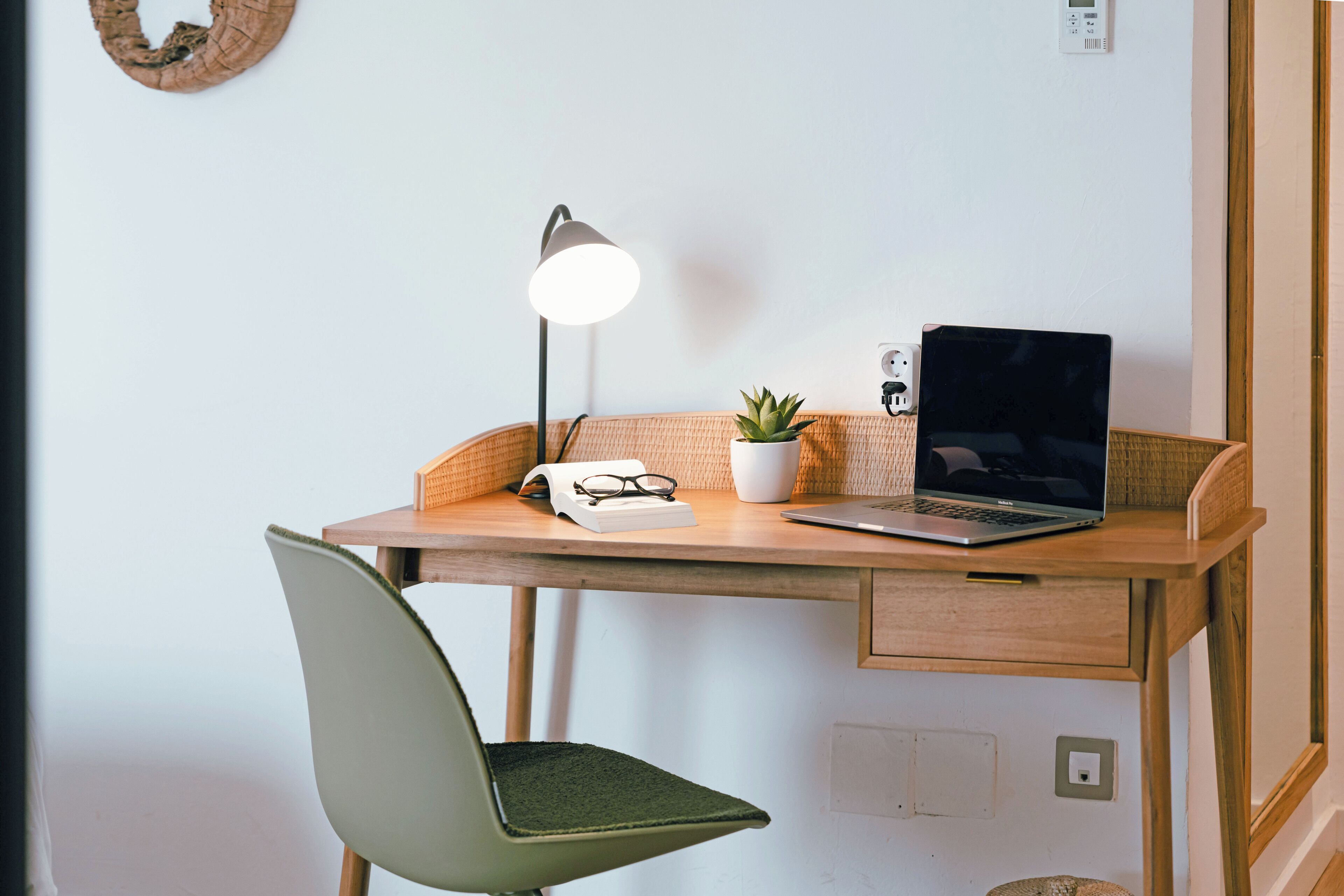 A workspace with a laptop, desk lamp, potted plant, and a chair.