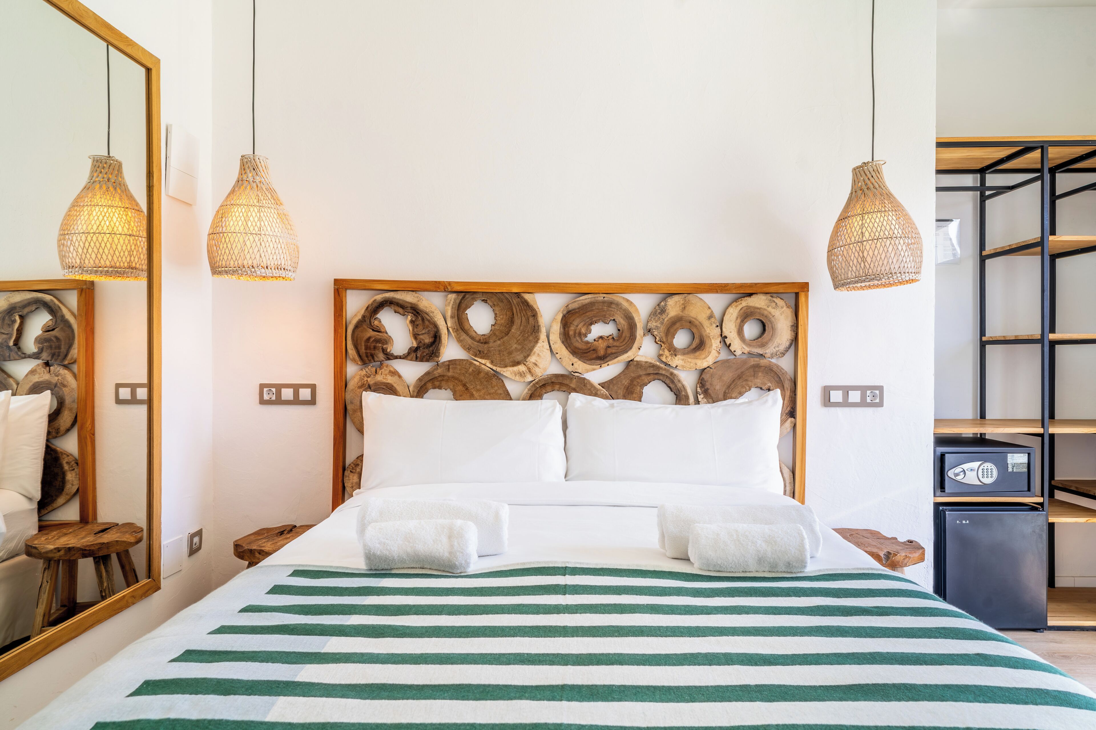 A hotel room with a bed, two bedside tables, a mirror, a wooden headboard, and two hanging light fixtures.