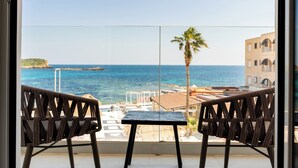 A balcony with two chairs and a small table, overlooking a beach with a palm tree and buildings in the background. - Outsite Ibiza - Work, Connect, Explore (Santa Eulalia del Rio)